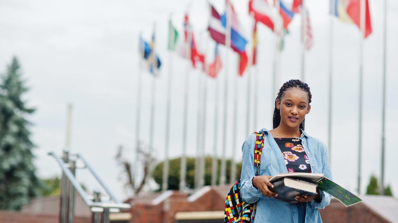 Young college student stands near many nations flags